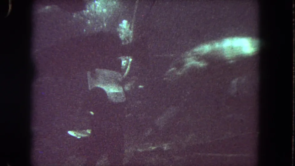 1962 Los Angeles 8mm underwater frame with a helmeted diver near the ocean floor and a large fish passing in low light.