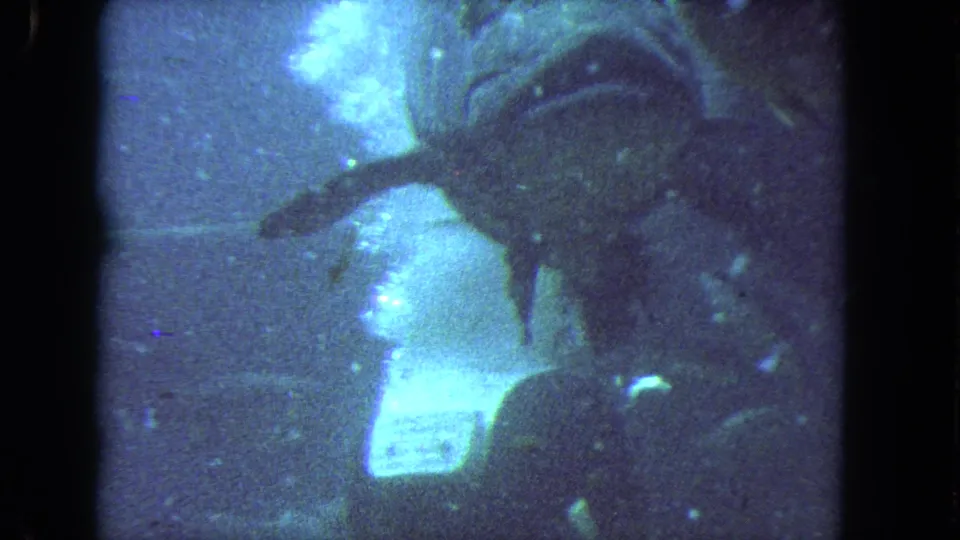 1962 Los Angeles 8mm frame of a scuba diver moving underwater, with bubbles rising and fish in the surrounding water.