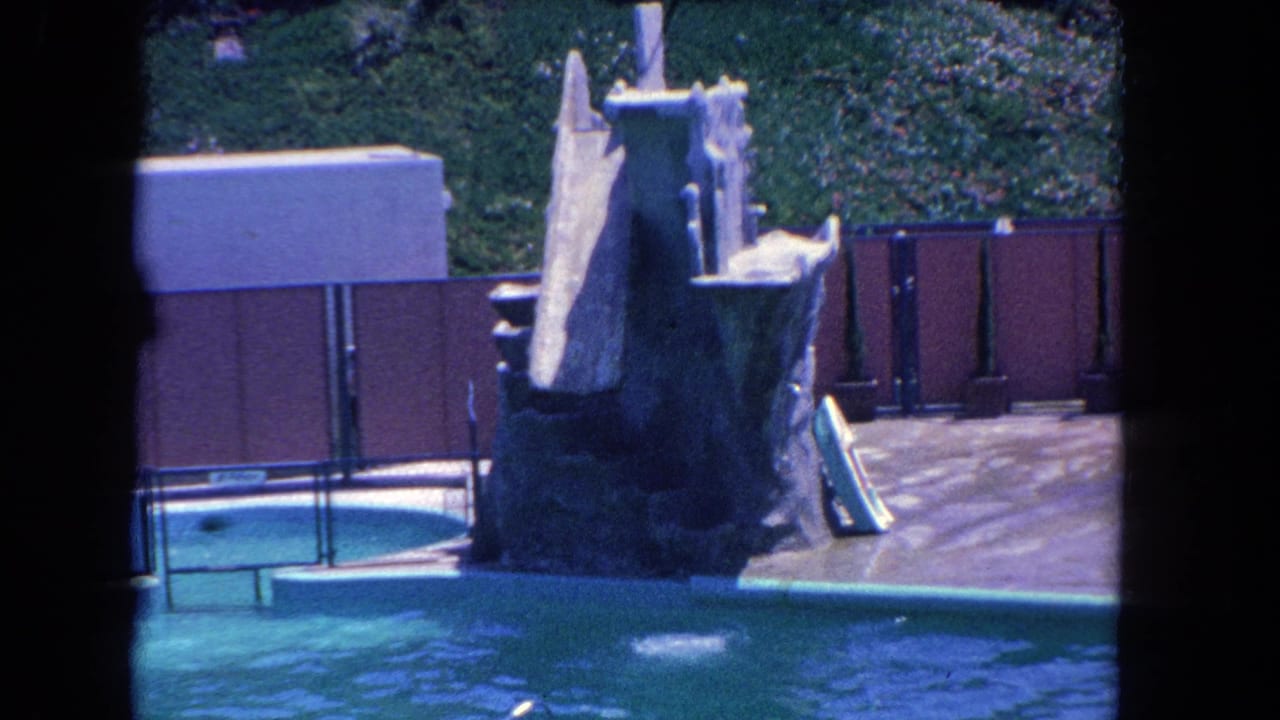 1962 Los Angeles 8mm frame showing a homemade robot figure near a pool, slide structure, deck, and fencing.