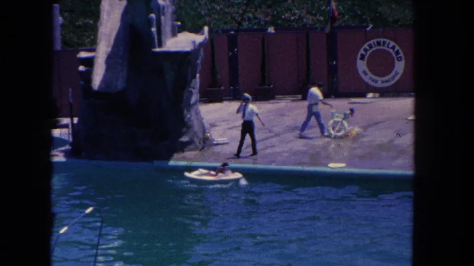 Visitor-shot 1962 Marineland footage shows trainers on the deck, a small boat in the pool, and a large artificial rock-like show feature.