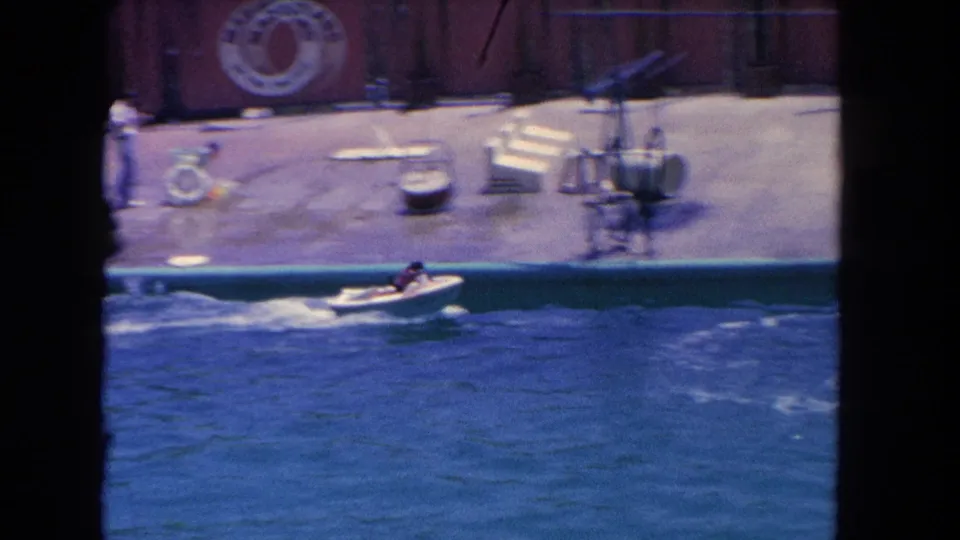 A small speedboat crosses the blue show pool in front of the Marineland deck, with deck equipment and signage visible behind it.