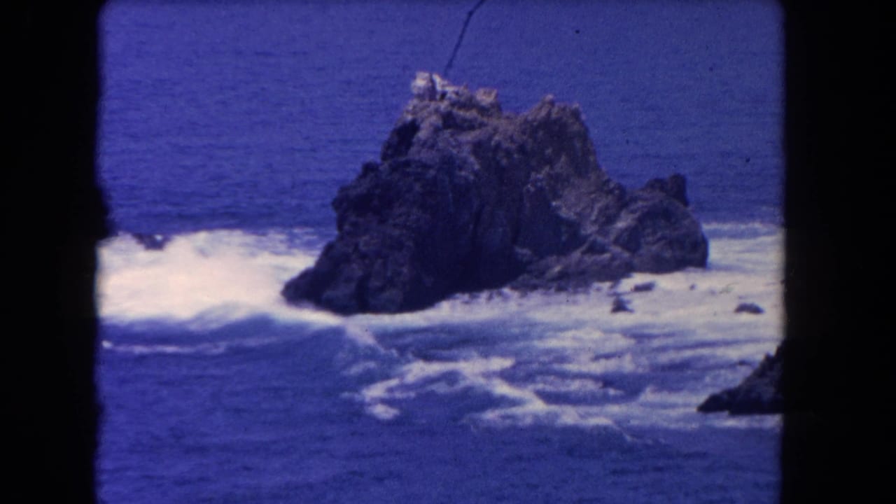 1962 8mm Los Angeles coastal footage showing waves breaking around a large jagged rock in blue water.