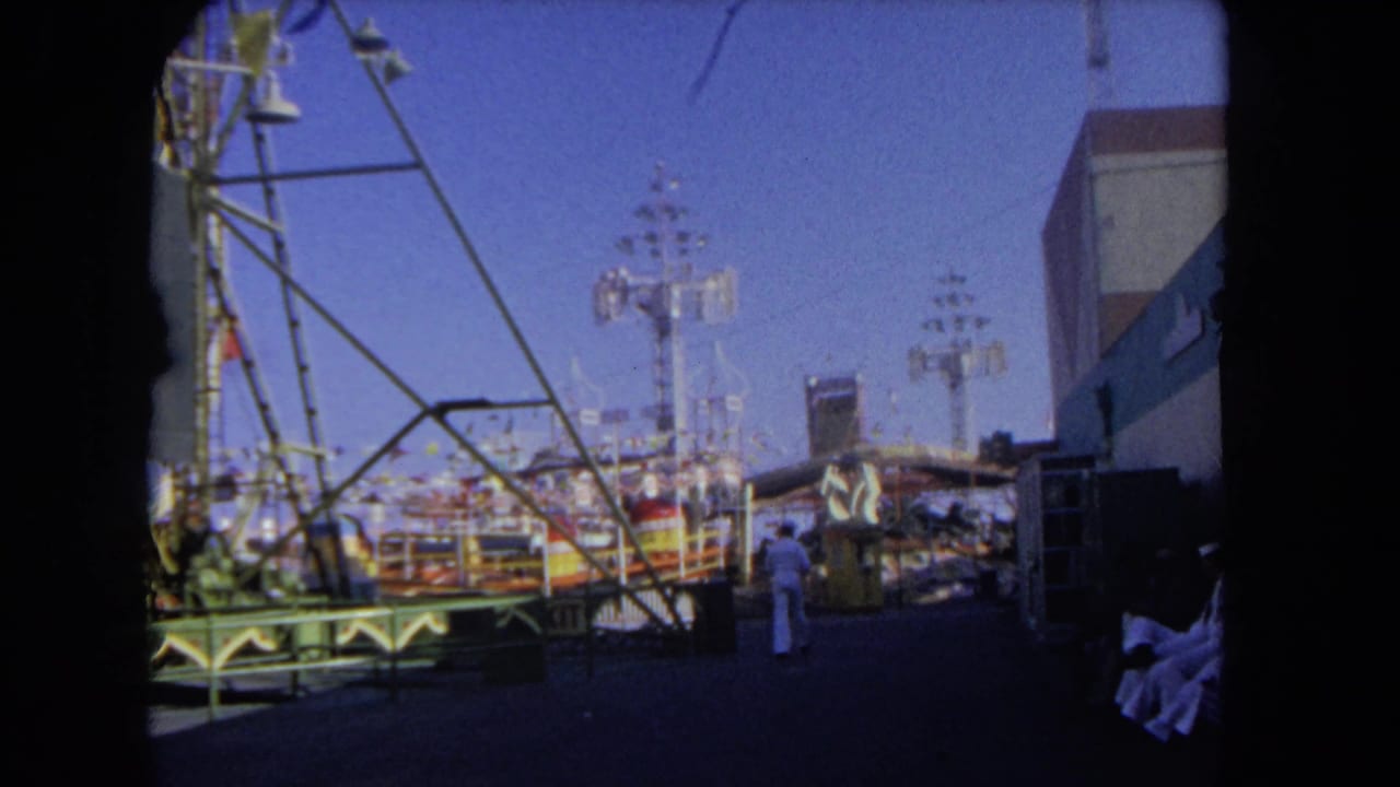1962 Los Angeles amusement park footage showing ride framework, midway structures, and a small visible visitor in white clothing.