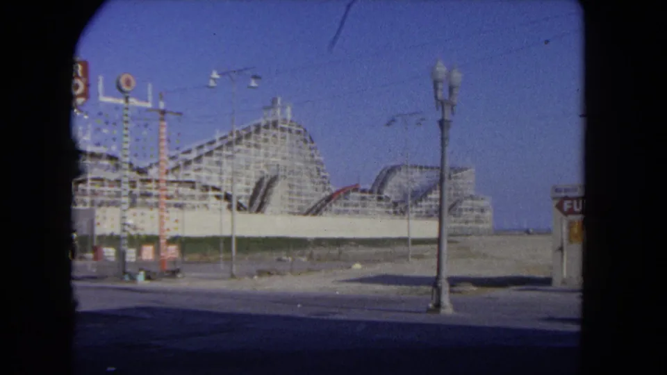 A visitor-shot 8mm view of the Los Angeles amusement park roller coaster, with midway lamps and dark film gate borders visible.