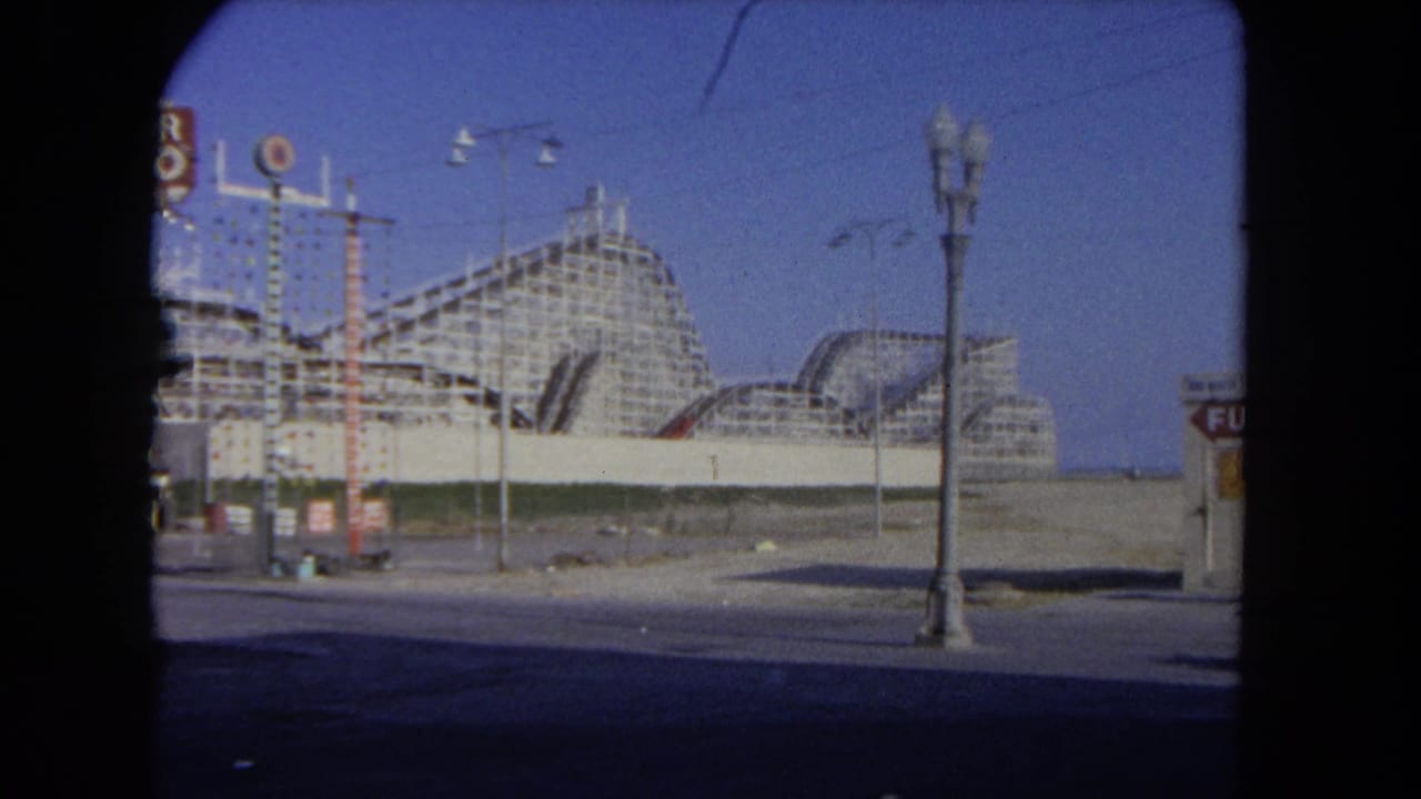 Wooden roller coaster structure behind a street and lamppost.