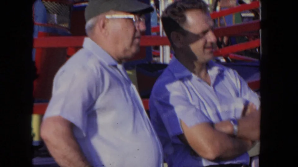 The final frame shows two men watching from beside a red-railed carnival ride in supported 1962 Los Angeles footage.
