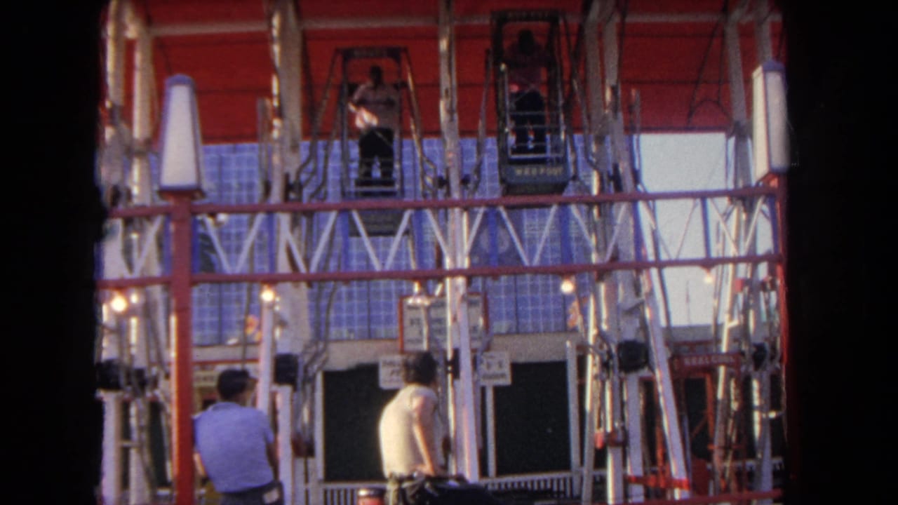 Ferris wheel station with red gondolas, railings, and people standing near the platform.