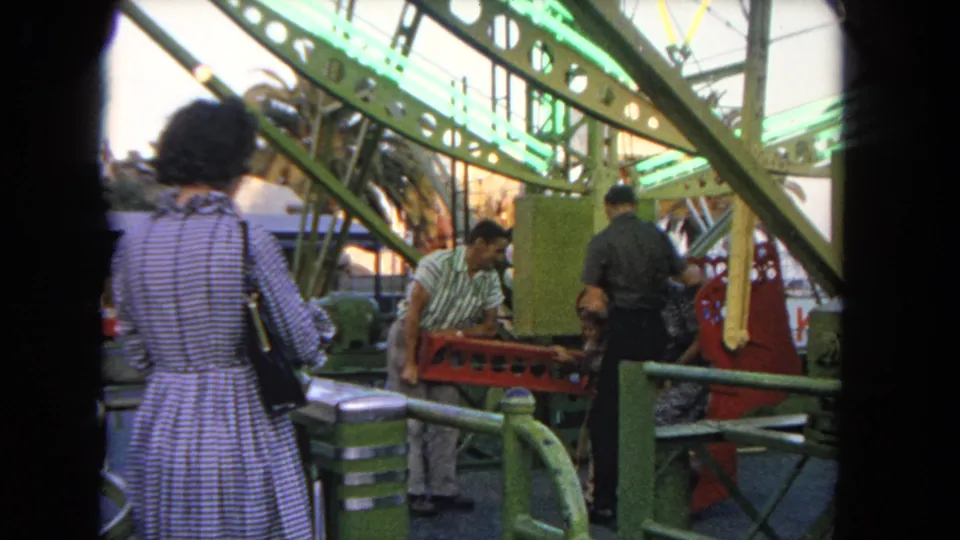 People gather around a red Ferris wheel gondola beneath green metal supports at a Los Angeles fairground in 1962.
