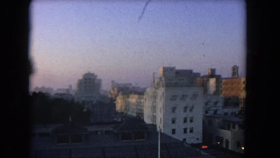 1962 Los Angeles-area skyline frame with rooftops, low-rise buildings, taller background structures, and dusk sky.