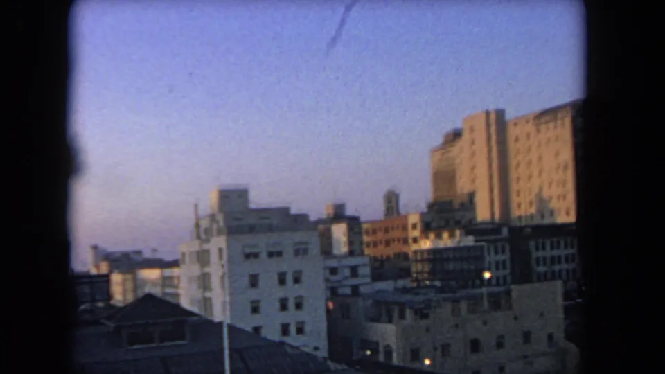 Los Angeles-area 1962 home-movie frame showing rooftops and mid-century city buildings in soft evening light.