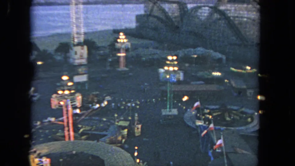 Elevated 1962 Los Angeles oceanside carnival view with ride lights, flags, small visitors, beach, and ocean in the background.