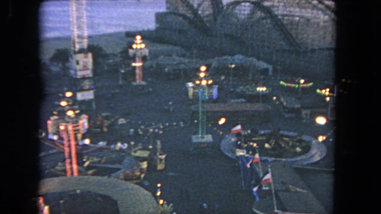 Elevated dusk view of an amusement park with ride lights and a wooden roller coaster.