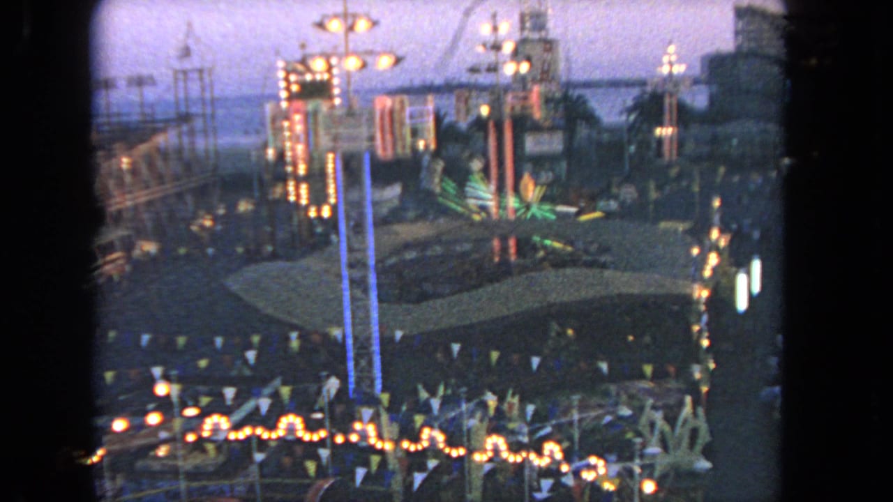 Elevated 1962 Los Angeles fairground view with lit booths, bunting, a roller coaster track, and crowds seen from a moving ride.