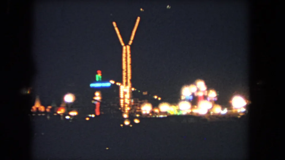 Nighttime 1962 Los Angeles fair footage showing a tall lighted tower, rows of bright bulbs, and distant amusement attractions.