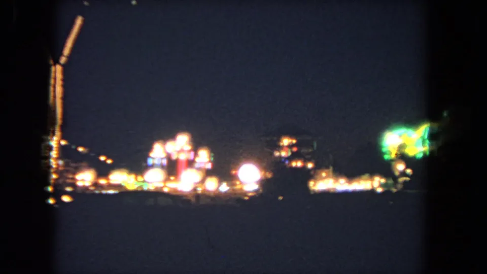 1962 Los Angeles 8mm frame showing soft fairground lights, a cropped illuminated tower, and a green glowing sign or ride light.