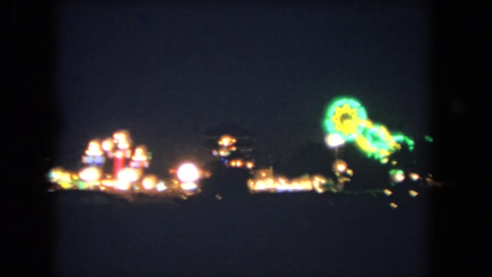 1962 Los Angeles nighttime frame with distant amusement lights and a bright green starburst-shaped sign or ride light.