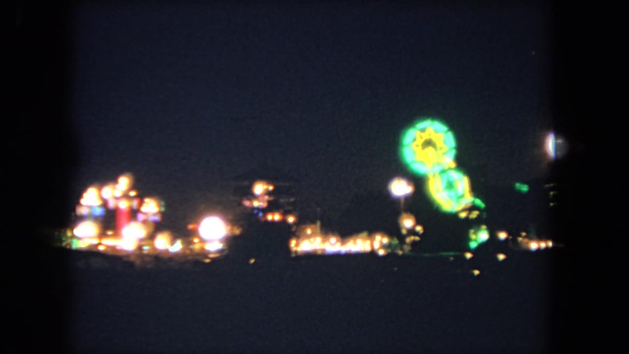 1962 Los Angeles 8mm frame showing blurred fairground lights and a green and yellow ride glowing against a dark sky.