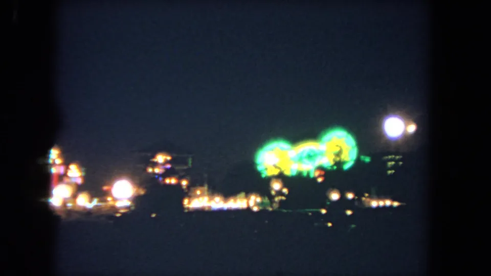 1962 Los Angeles 8mm frame showing a soft-focus carnival ride with green lights amid warm out-of-focus midway bulbs.