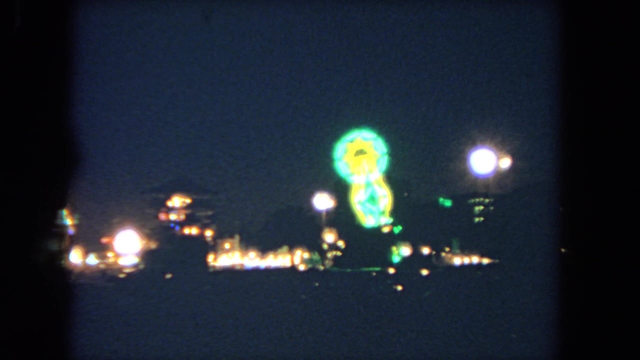 Night roadway lights and a bright green roadside sign seen through dark 8mm film borders.