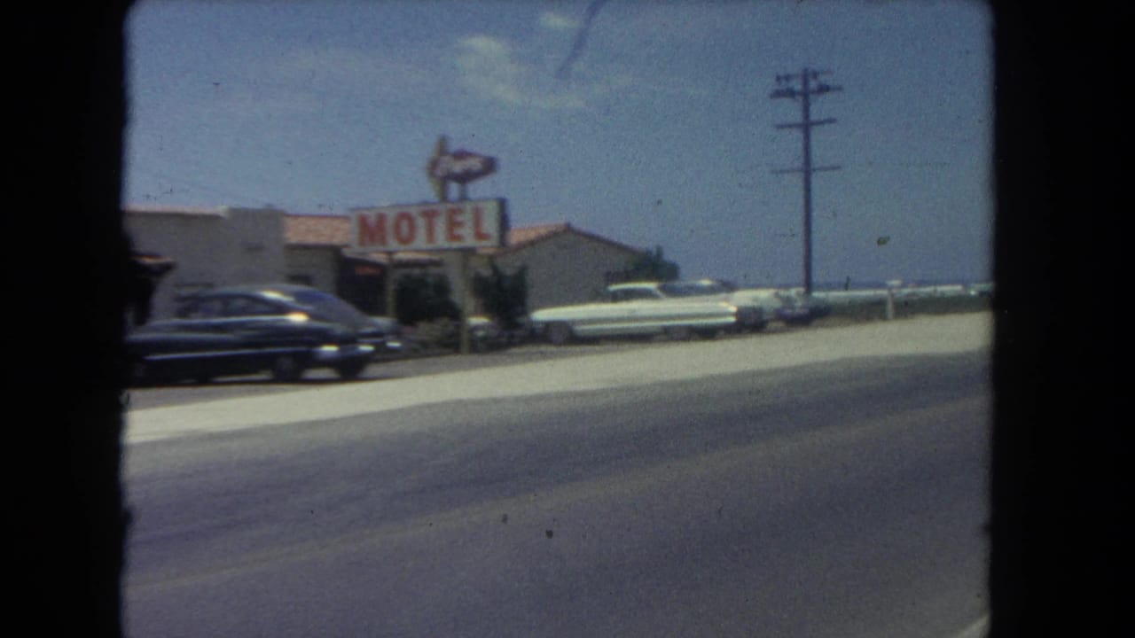 Roadside motel sign, parked cars, utility pole, and beachside road under a blue sky.