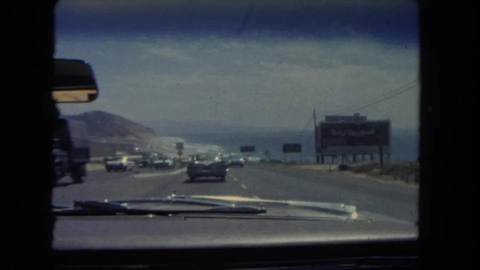 1962 Los Angeles passenger-view footage shows cars on a coastal highway with the Pacific Ocean to the right and billboards along the road.