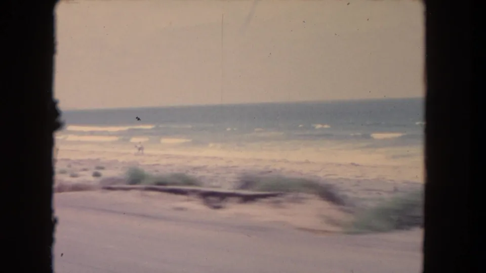 Brief 1962 coastal view from a moving car, showing ocean waves and shoreline through soft home-movie motion blur.