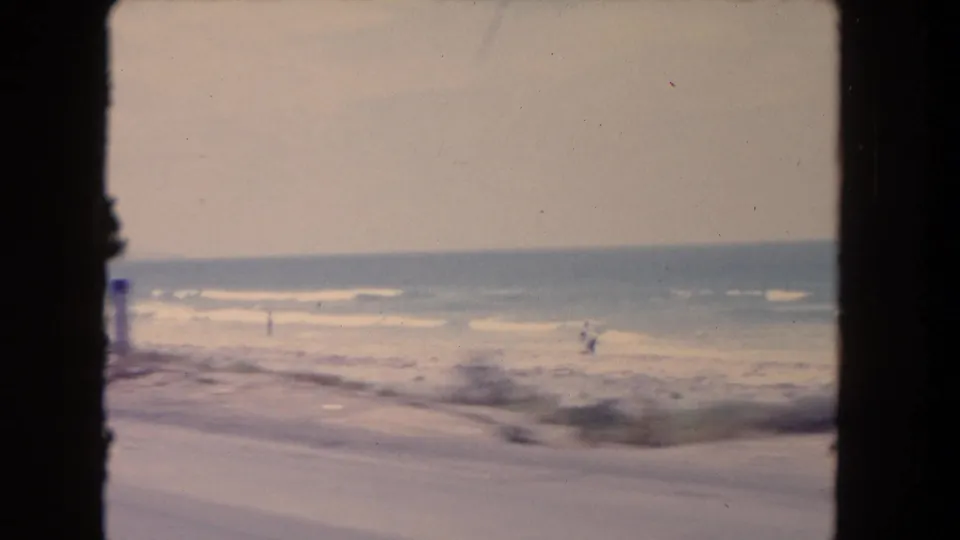 Soft 8mm beach view in Los Angeles metadata, with surf, sand, haze, and small distant figures near the waterline.
