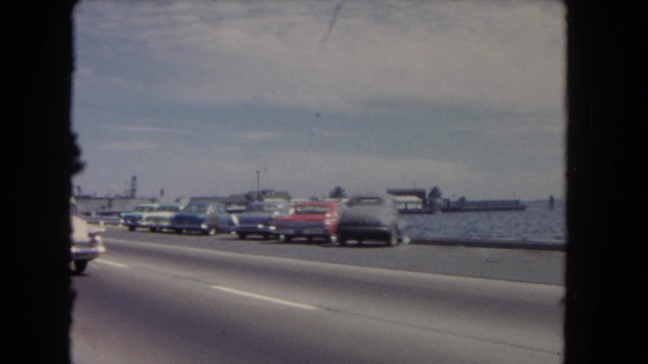 Several cars drive beside the water, including a red convertible.