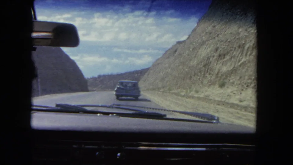 Interior car viewpoint from 1962 showing a sedan ahead on a paved mountain pass road in the Los Angeles area.