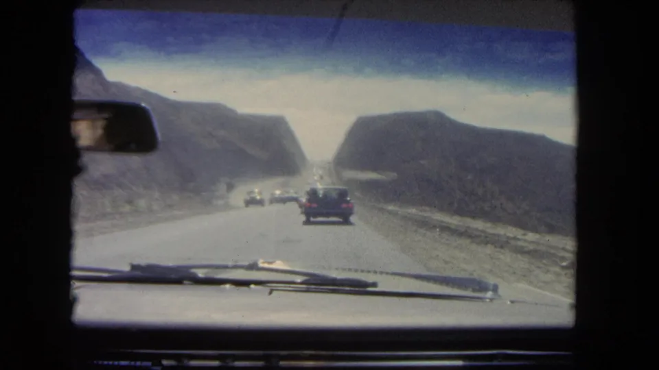 1962 8mm home-movie view through a vehicle windshield, with several cars traveling through a rocky California pass.