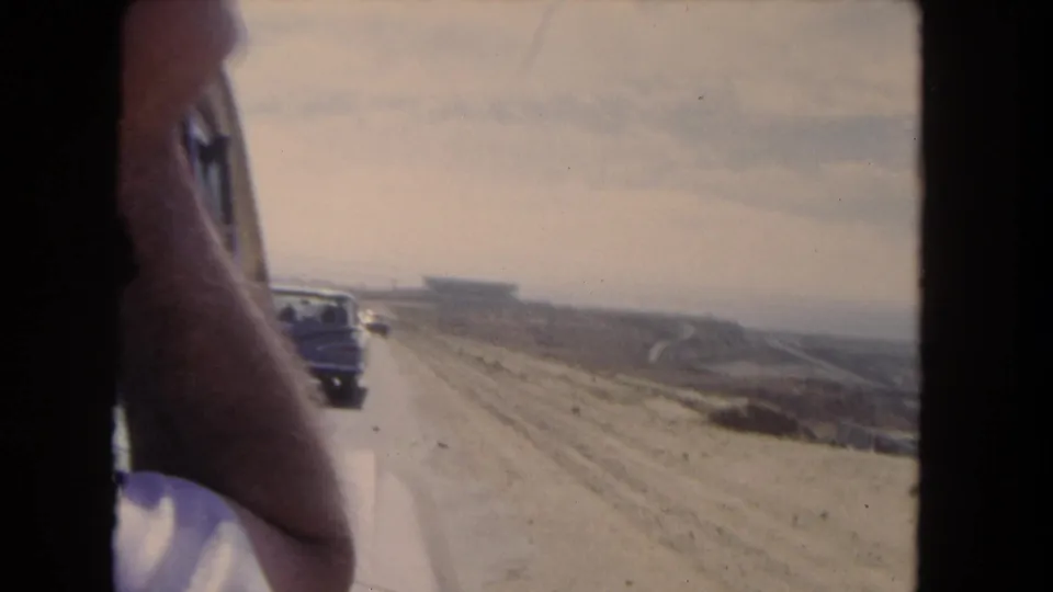 1962 Los Angeles-area home-movie frame showing cars on a dusty road from a moving passenger-side viewpoint.