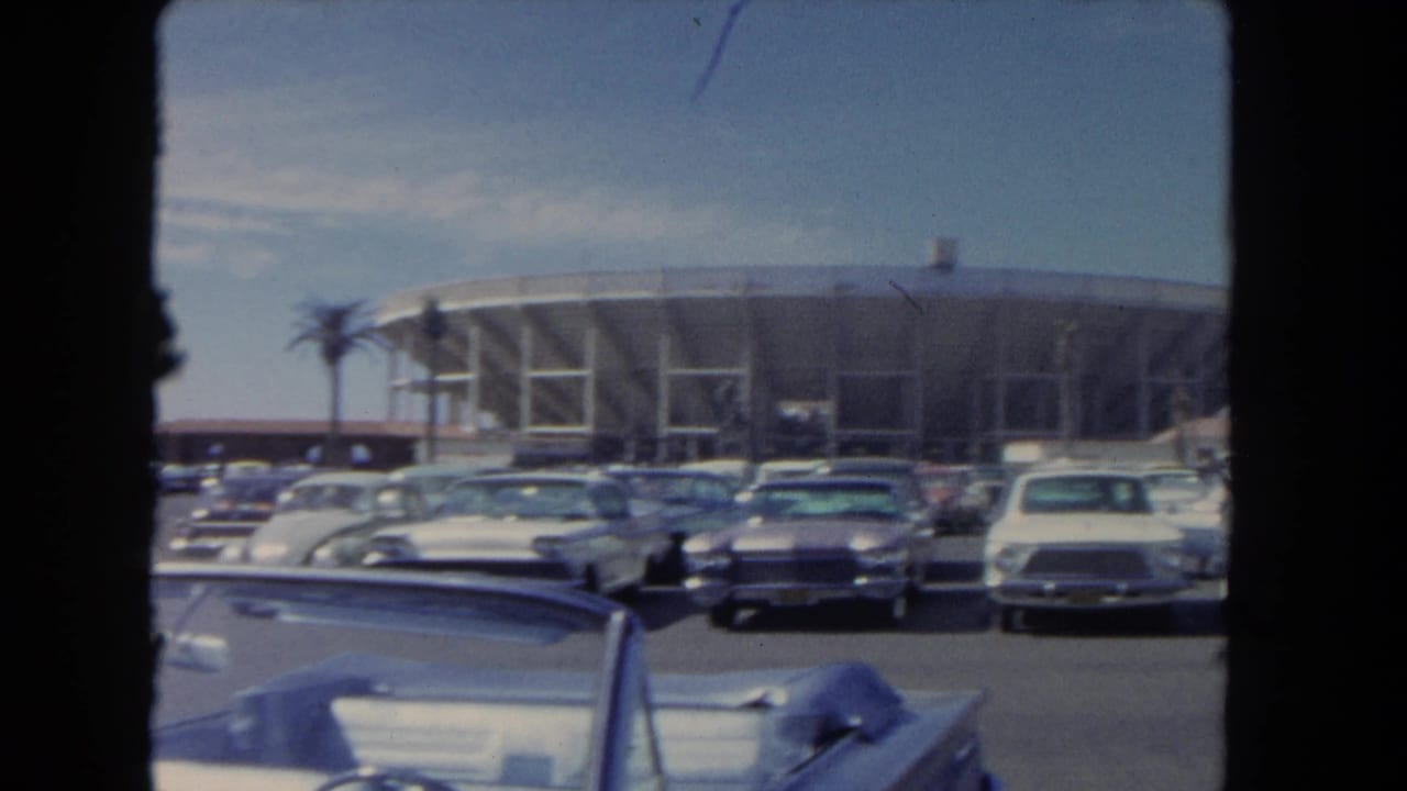 1962 Los Angeles view of classic cars in a parking lot facing a large modern arena or stadium exterior.