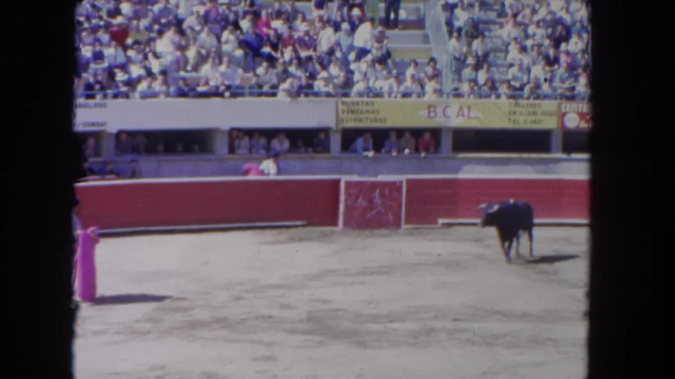 A matador holding a pink cape faces a black bull across the sunlit Los Angeles arena.