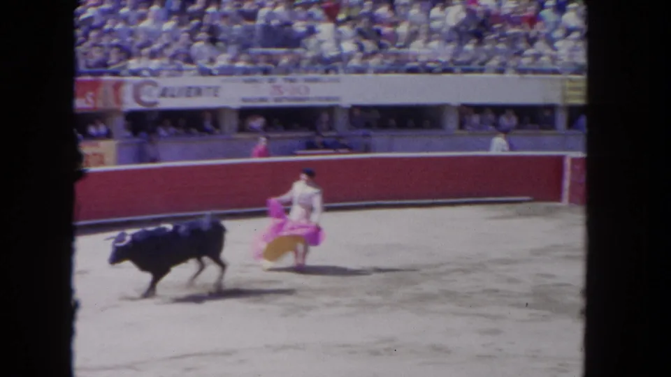 A matador in a light suit uses a pink cape as a black bull charges across the Los Angeles arena.