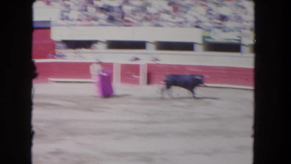 Soft 8mm frame from the Los Angeles arena scene, with the matador and pink cape near a dark bull in motion.
