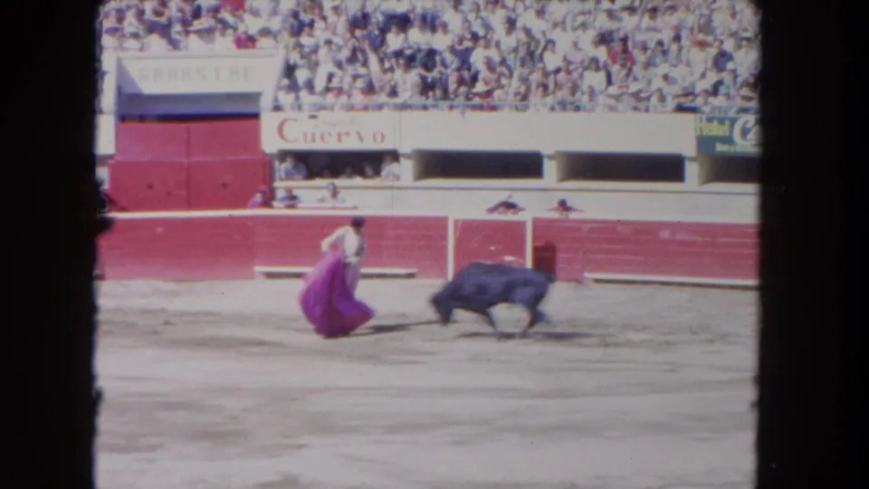 1962 Los Angeles arena frame showing a matador crouching with a pink cape while a dark bull passes close by.