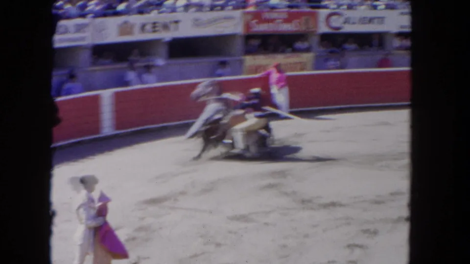 1962 Los Angeles 8mm frame showing a matador with a pink cape near a charging bull and horse in a crowded arena.