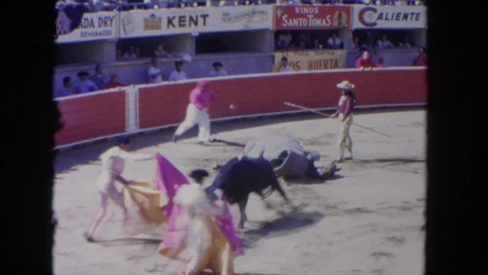 1962 Los Angeles 8mm frame showing a bull down in the arena while matadors with capes and handlers stand or rush nearby.