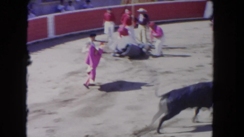 1962 Los Angeles 8mm frame with a matador crossing the sand while men gather around a bull lying near the arena barrier.