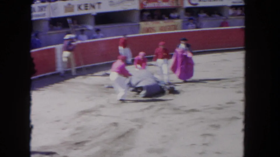 1962 Los Angeles bullfight frame showing handlers and matadors surrounding a bull on the sand as spectators watch from the stands.