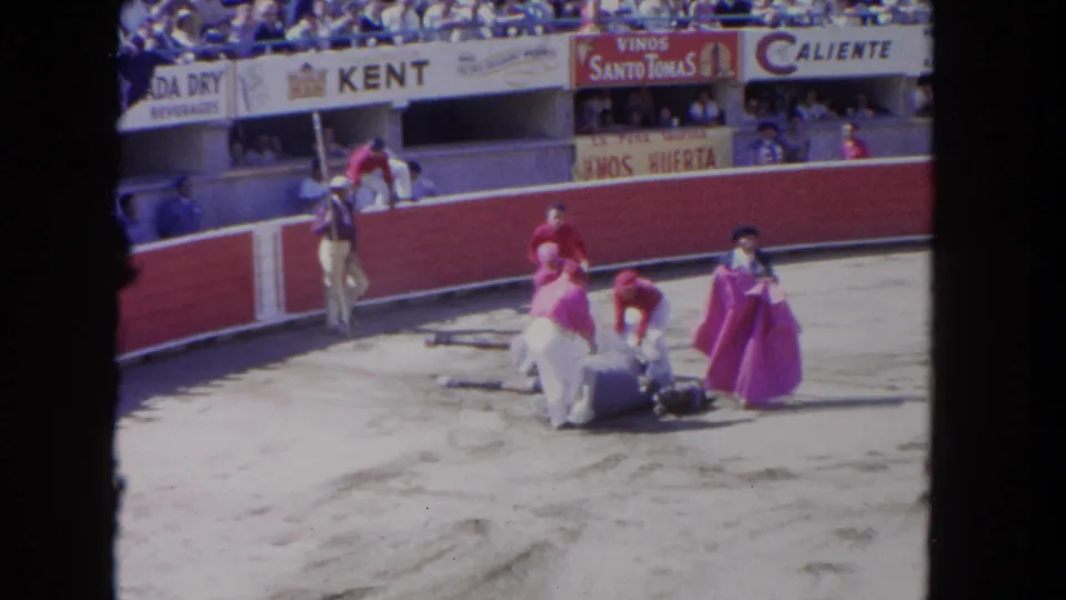 1962 Los Angeles 8mm frame showing handlers and matador-style performers around a fallen horse inside a crowded arena.