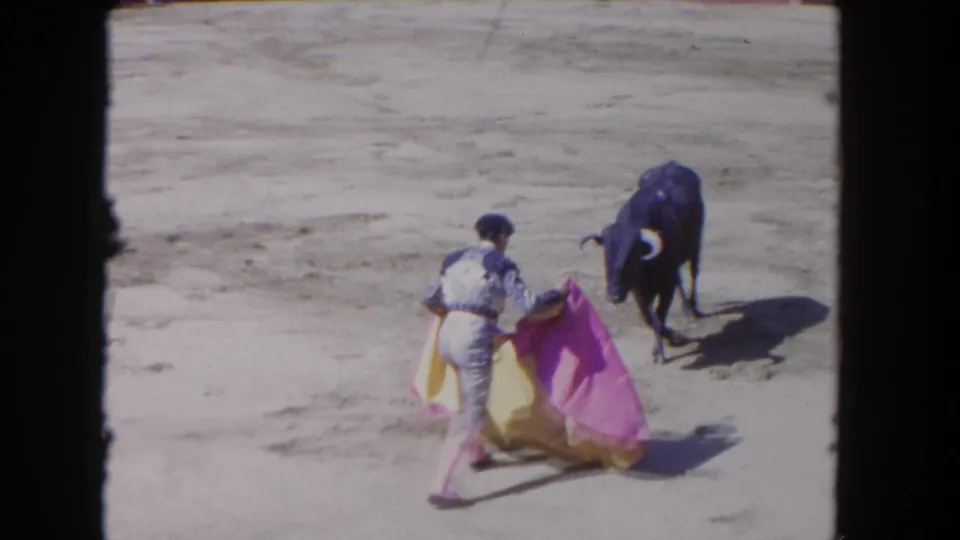 Matador in a sunlit Los Angeles arena appears to draw a black bull toward a pink and yellow cape during the 1962 8mm clip.