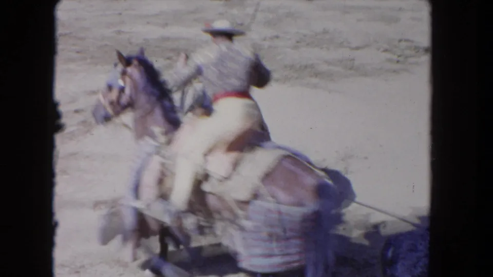 Motion-blurred 1962 Los Angeles 8mm frame of a cowboy on horseback passing close by with a long lance in the arena.