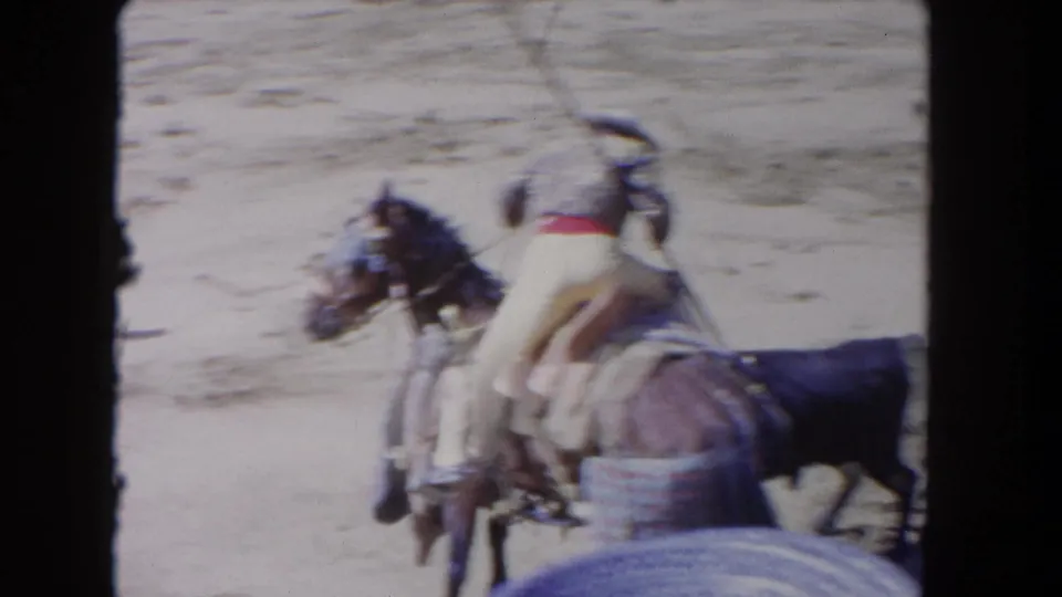 1962 Los Angeles 8mm frame showing mounted bullfighters in a sandy bullring beside a dark bull, with soft focus and visible film edges.