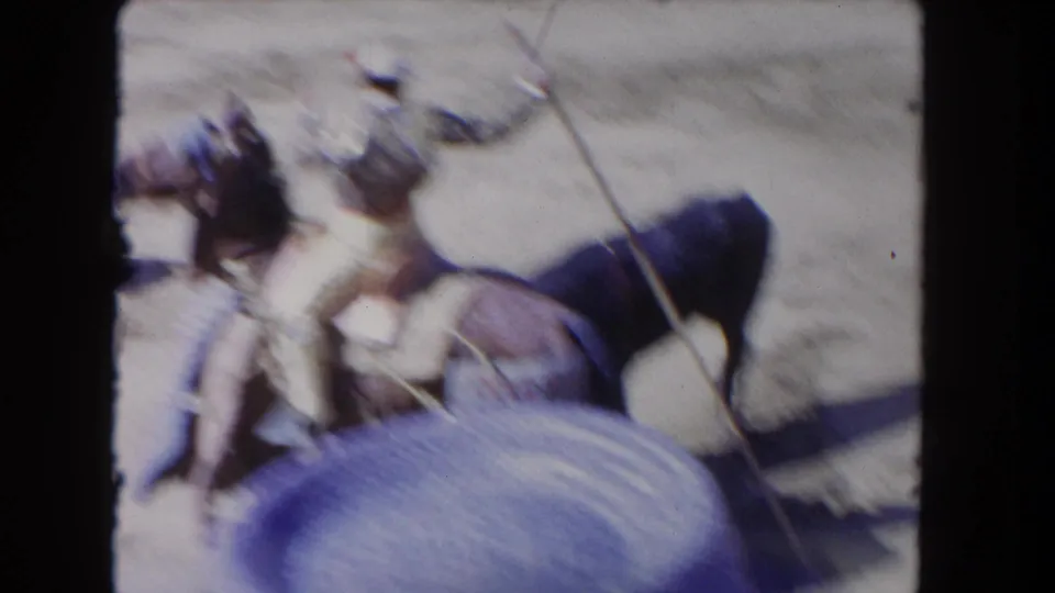 Blurred 8mm frame of mounted bullfighters with lances moving near a dark bull in the Los Angeles arena setting.
