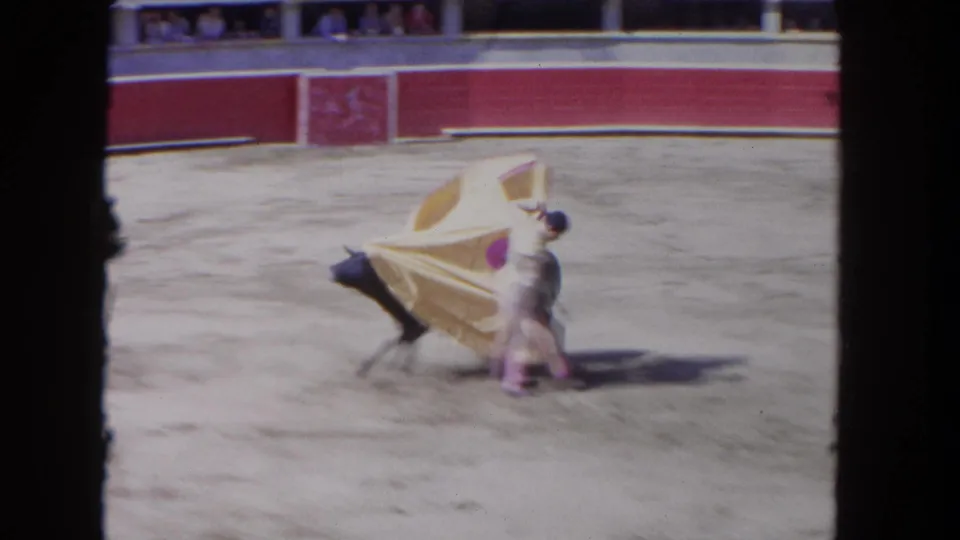 8mm frame from the Los Angeles bullfighting scene with a bullfighter sweeping a yellow and pink cape as a dark bull charges close.