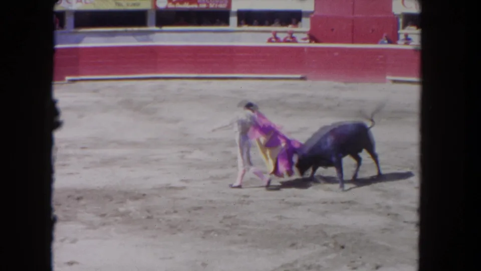 1960s 8mm frame of a bull passing close to a bright cape held by a performer in a bullring.