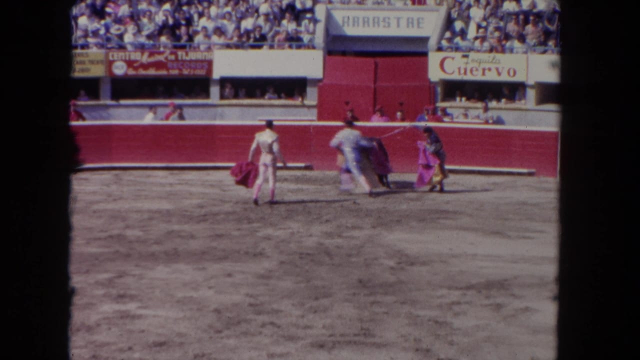 Two matadors with capes engaging a bull in a sunlit arena, circa 1962; José Cuervo tequila branding and ARRASTRE banner visible on arena stands — likely a Tijuana venue.