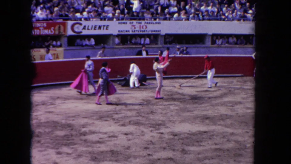 8mm home-movie frame circa 1962 showing multiple corrida participants gathered in the ring beneath Caliente and Vinos Santo Tomas banners.