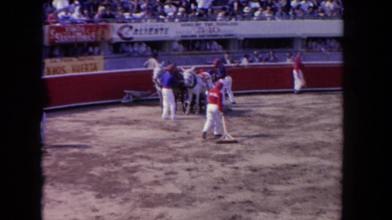 Arena crew and horse-drawn drag cart on the floor of what may be a Tijuana bullring circa 1962, with Caliente and Vinos Santo Tomás signage on the red barrera.